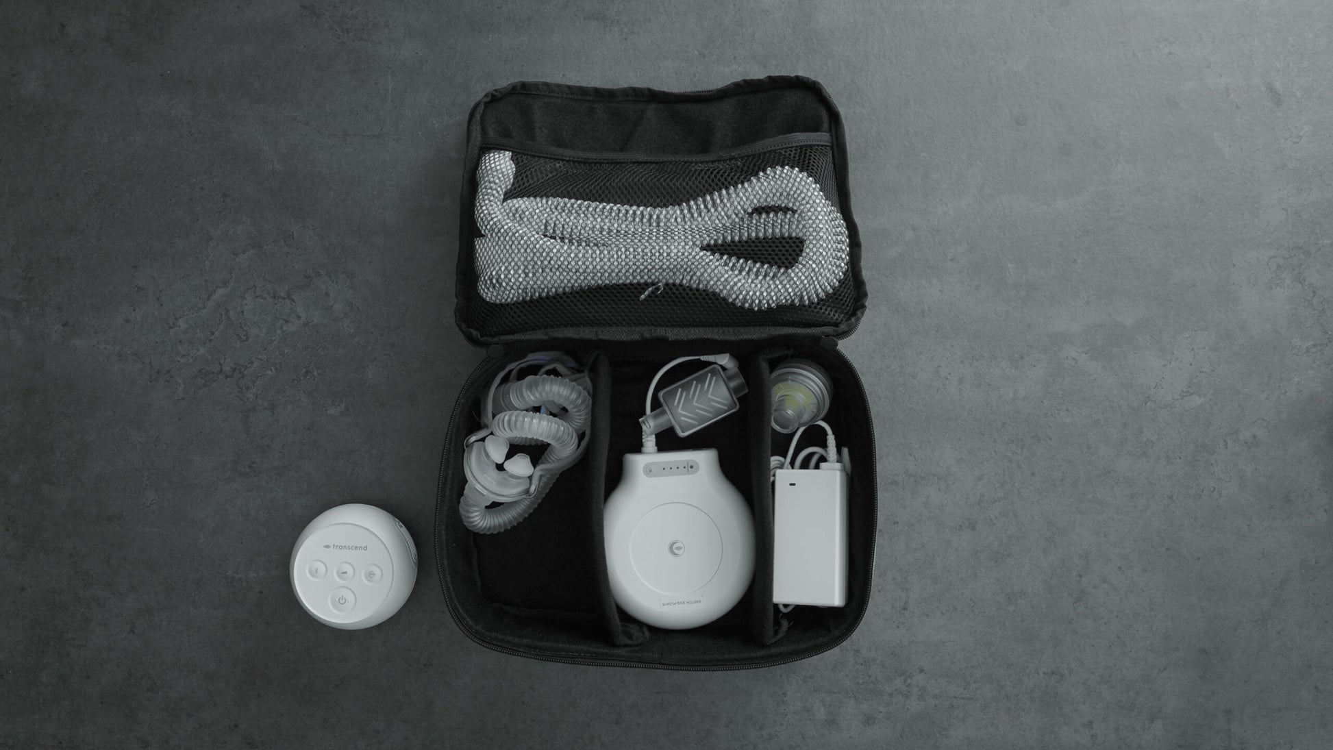 Transcend Micro travel bag opened with accessories neatly stored inside, including tubing, mask, battery, and charger, with the Transcend Micro machine placed outside of the case.